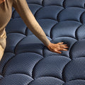A hand pressing into the scalloped quilted surface of a DreamCloud Luxe 14-inch mattress to demonstrate responsive memory foam contouring.
