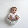 Baby resting on the textured surface of an organic mini crib mattress in a top view.