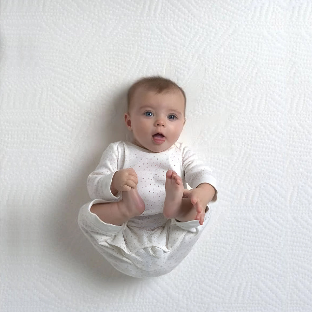 Baby resting on the textured surface of an organic mini crib mattress in a top view.