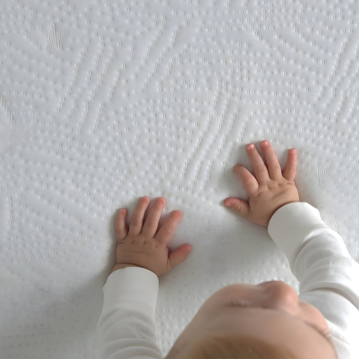 Close-up of a baby's hands feeling the soft, quilted texture of an organic mini crib mattress.