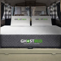 Modern camper van bedroom interior featuring a GhostBed RV 10-inch mattress styled with neutral bedding and decor.
