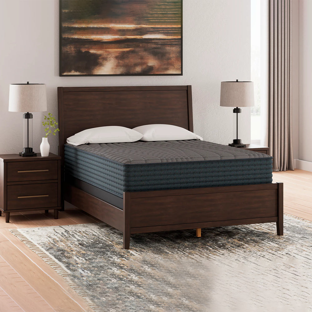 Full view of the Ashley Gray 1200 Hybrid 12-inch mattress on a dark wood platform bed frame with a designer rug and master bedroom decor.
