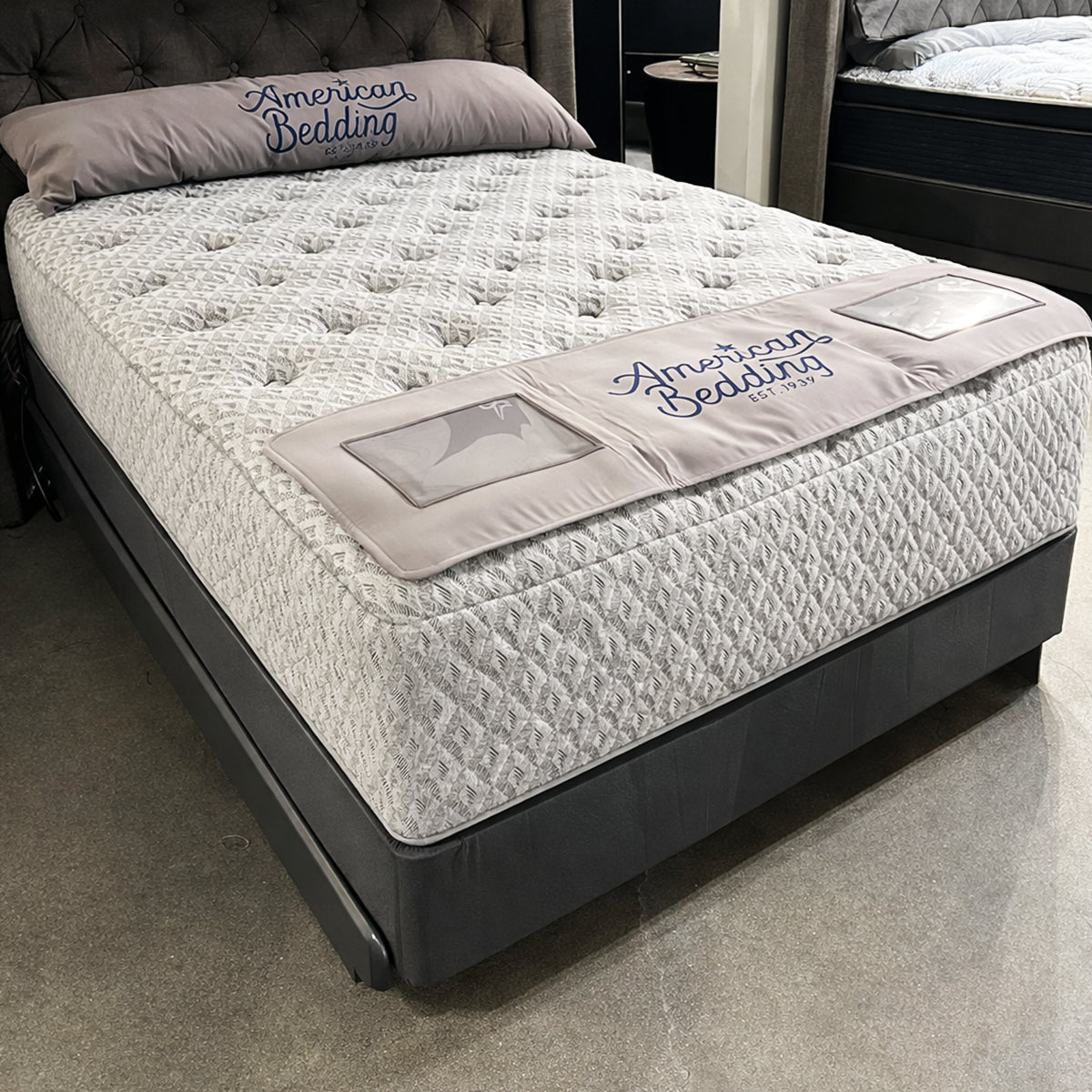 American Bedding Anabella 14" Mattress in showroom view featuring a plush tufted top and grey upholstered base.