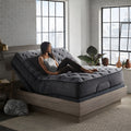 Nights Bridge 12-inch plush hybrid mattress by Corsicana elevated on an adjustable power base in a modern bedroom with large windows.
