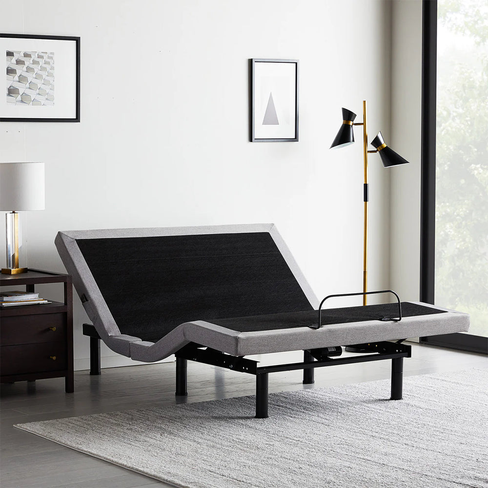 Malouf M555 adjustable bed base in a modern bedroom setting with head and foot sections elevated for ergonomic comfort.
