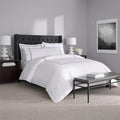 White SleepTone Hotel Luxury sheet set with grey double-stripe embroidery in a modern bedroom.

