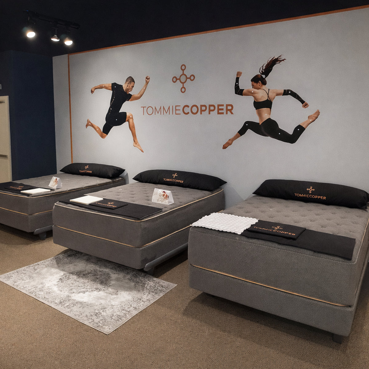 Retail showroom display of the Tommie Copper Sleep System mattresses featuring branded wall graphics highlighting athlete recovery and performance.

