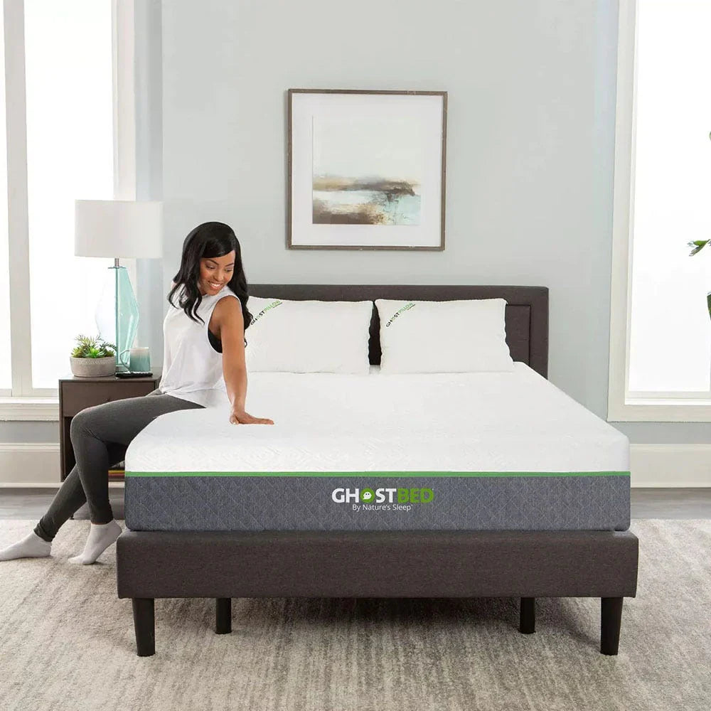 A woman sitting on the edge of a GhostBed Elite memory foam mattress, demonstrating the mattress's edge support and 12-inch medium comfort profile.
