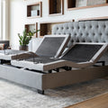 Split king Malouf M555 adjustable bed base in a lifestyle bedroom with a grey tufted headboard and articulated head sections.
