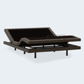 Three-quarter view of the Ashley Comfort Ultra motorized bed base showing charcoal grey upholstery and sturdy steel legs.

