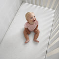 Happy toddler on a BEDGEAR Dri-Tec crib mattress protector providing a breathable, waterproof, and clean sleep.
