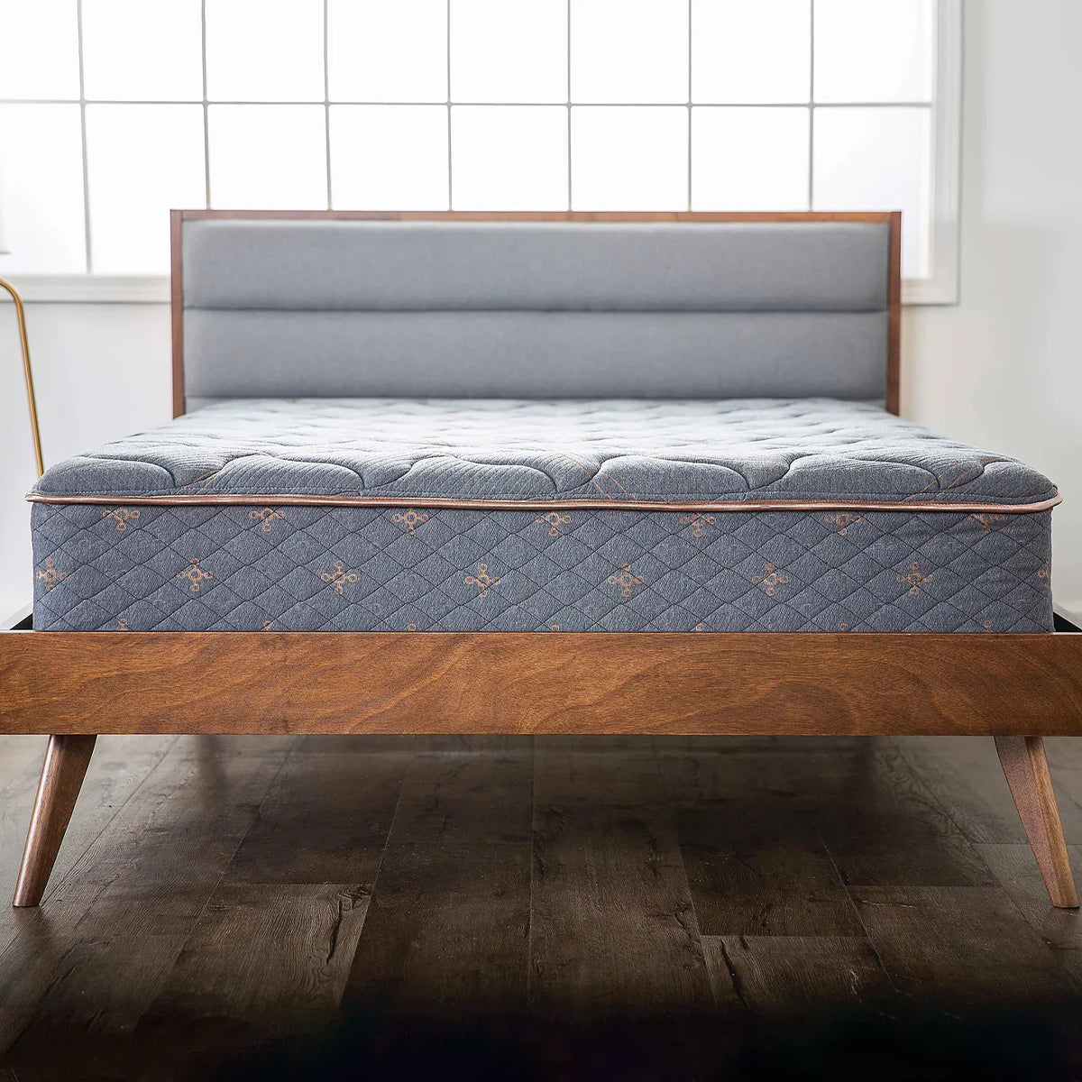 Front-facing view of the Tommie Copper Core Znergy 14-inch mattress styled on a mid-century modern wooden bed frame in a bright bedroom.
