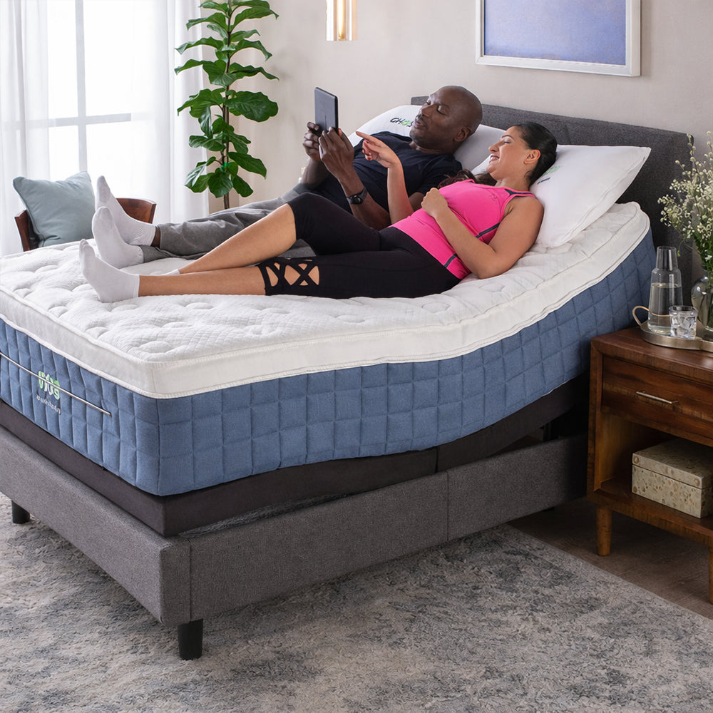 Couple relaxing on a GhostBed Performance 14-inch mattress with the head section elevated on an adjustable power base for reading and ergonomic sleep.
