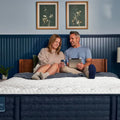 Couple sitting on a Serta iComfortPRO Ambrose firm mattress, showing motion isolation and cooling comfort.
