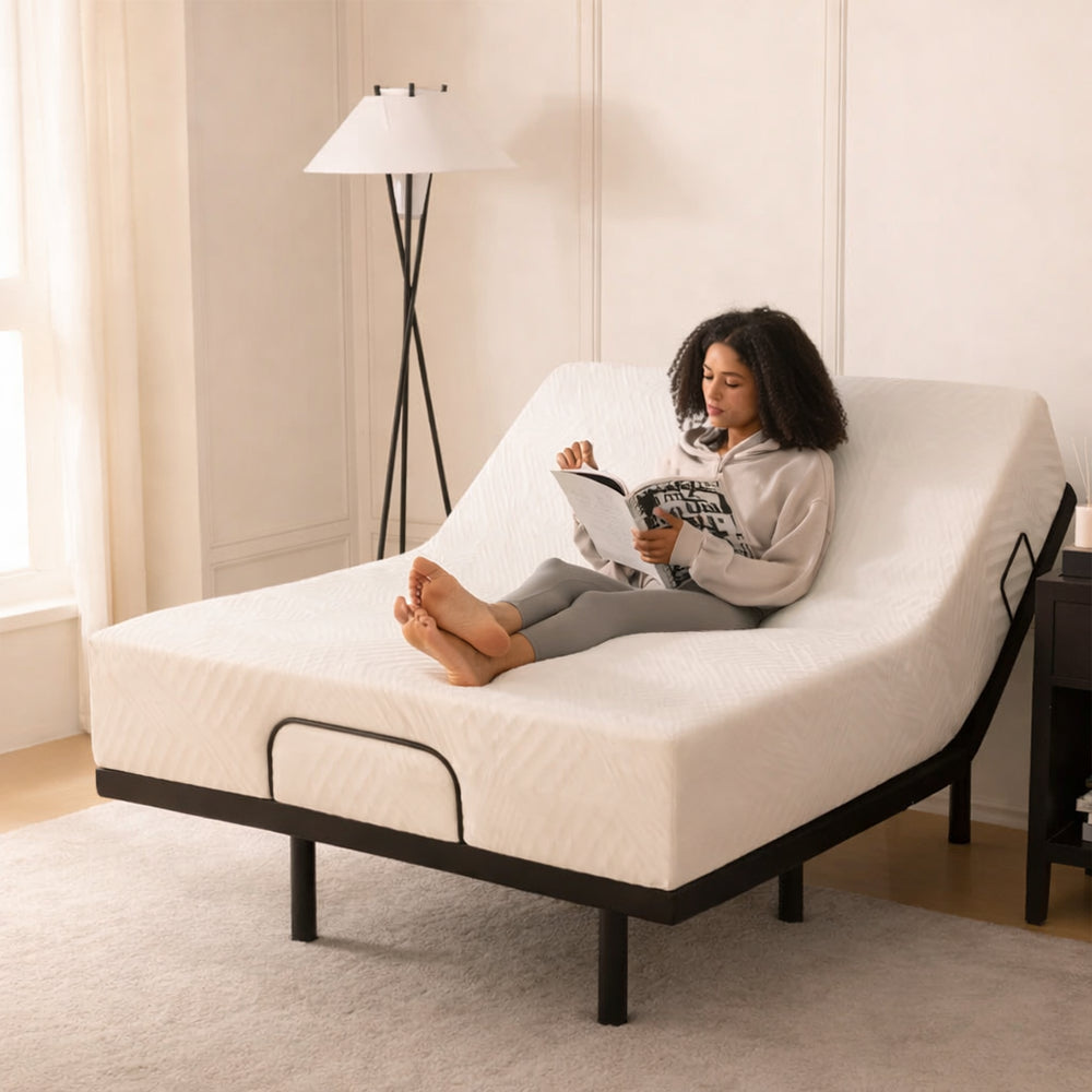Lifestyle bedroom view of a woman sitting on an MLILY MS 300 adjustable bed base with the head elevated for comfortable reading.

