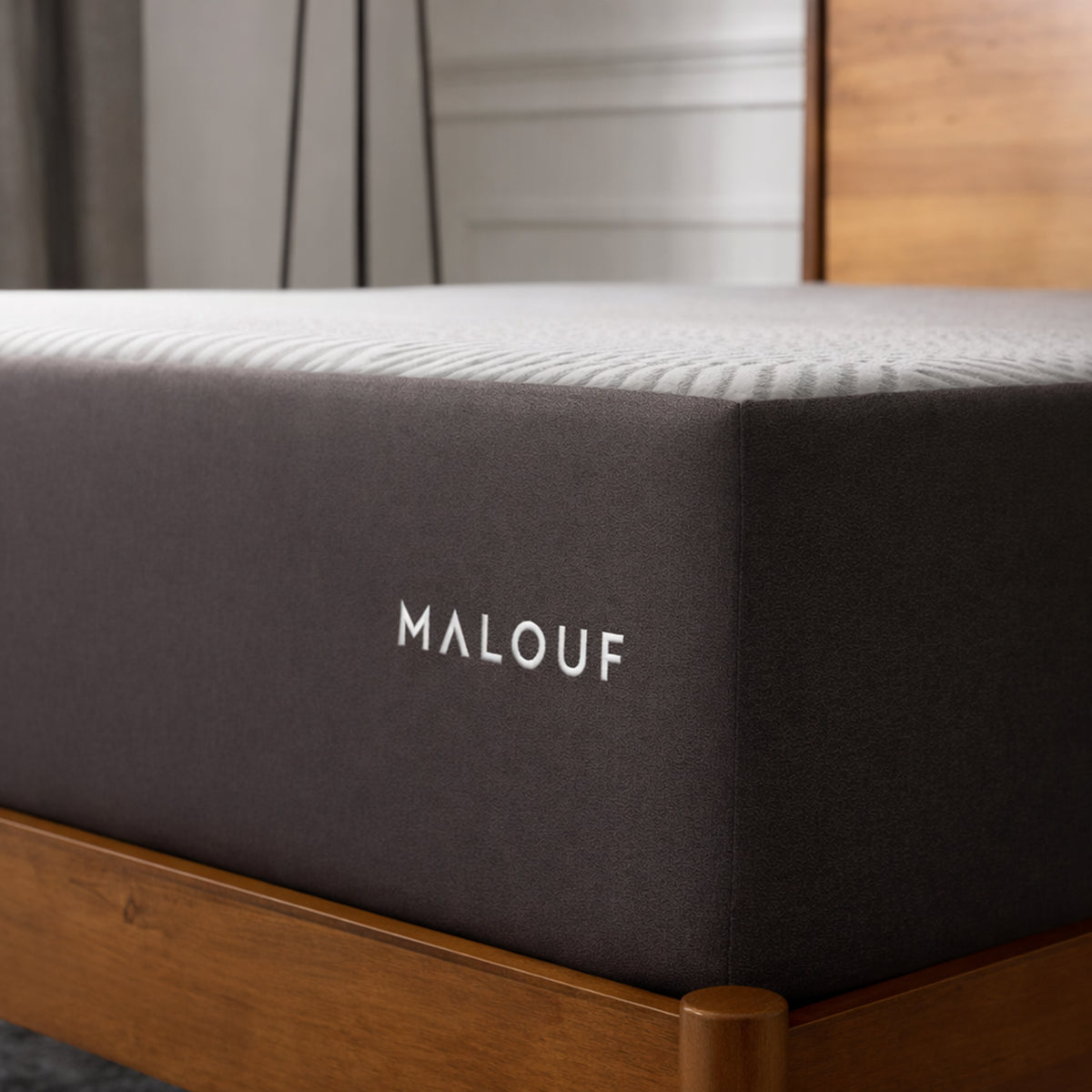 Side view of the Neve 10" Activair All-Foam Mattress on a wooden bed frame highlighting the Malouf embroidered logo.