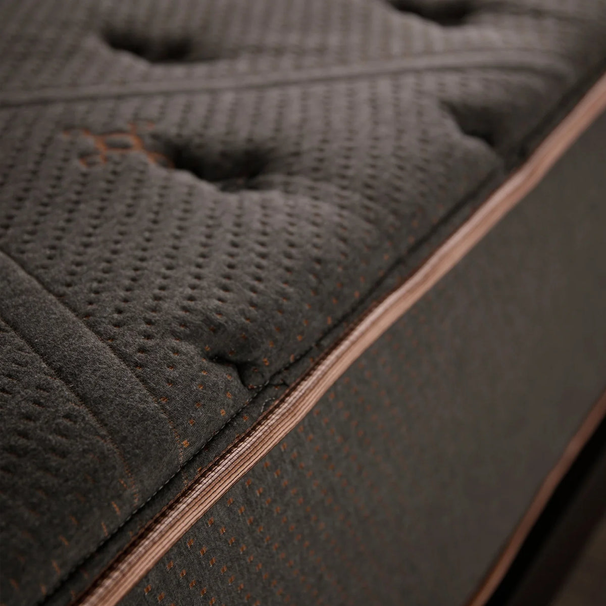Detailed close-up of the charcoal grey quilted surface and copper-toned piping of the Tommie Copper Core Znergy recovery mattress.
