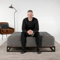 A man sitting on a Tommie Copper Core Znergy mattress showcasing the 14-inch profile and reinforced edge support.

