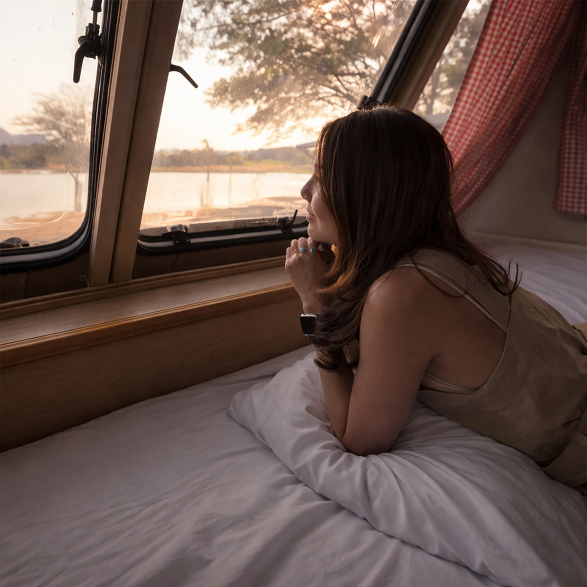 Traveler reclining on a GhostBed RV hybrid mattress looking out a camper window, emphasizing luxury road trip comfort.
