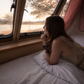 Traveler reclining on a GhostBed RV hybrid mattress looking out a camper window, emphasizing luxury road trip comfort.
