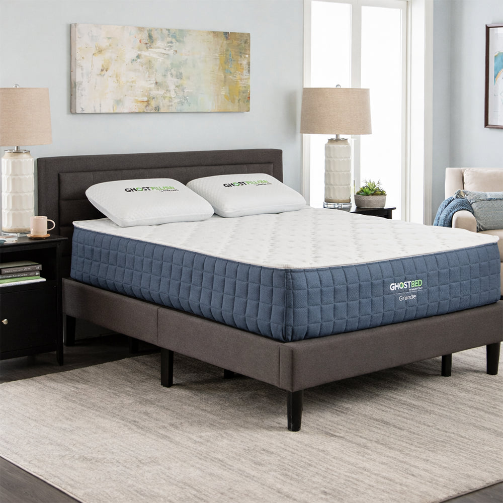 GhostBed Grande 14-inch medium mattress in a modern master bedroom setting, featuring blue quilted sides and GhostPillows on a grey platform frame.
