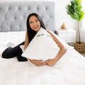 Woman hugging a GhostPillow shredded foam cooling pillow in a bright bedroom for cozy sleep comfort.
