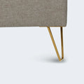 Close-up of the elegant gold hairpin legs and grey textured fabric on the Zoey upholstered platform bed.
