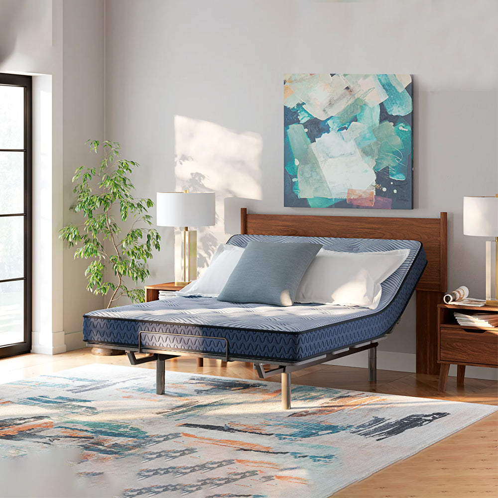 Ashley Peak 2.0 mattress with the head section elevated on an adjustable base in a modern sunlit bedroom with wooden furniture.
