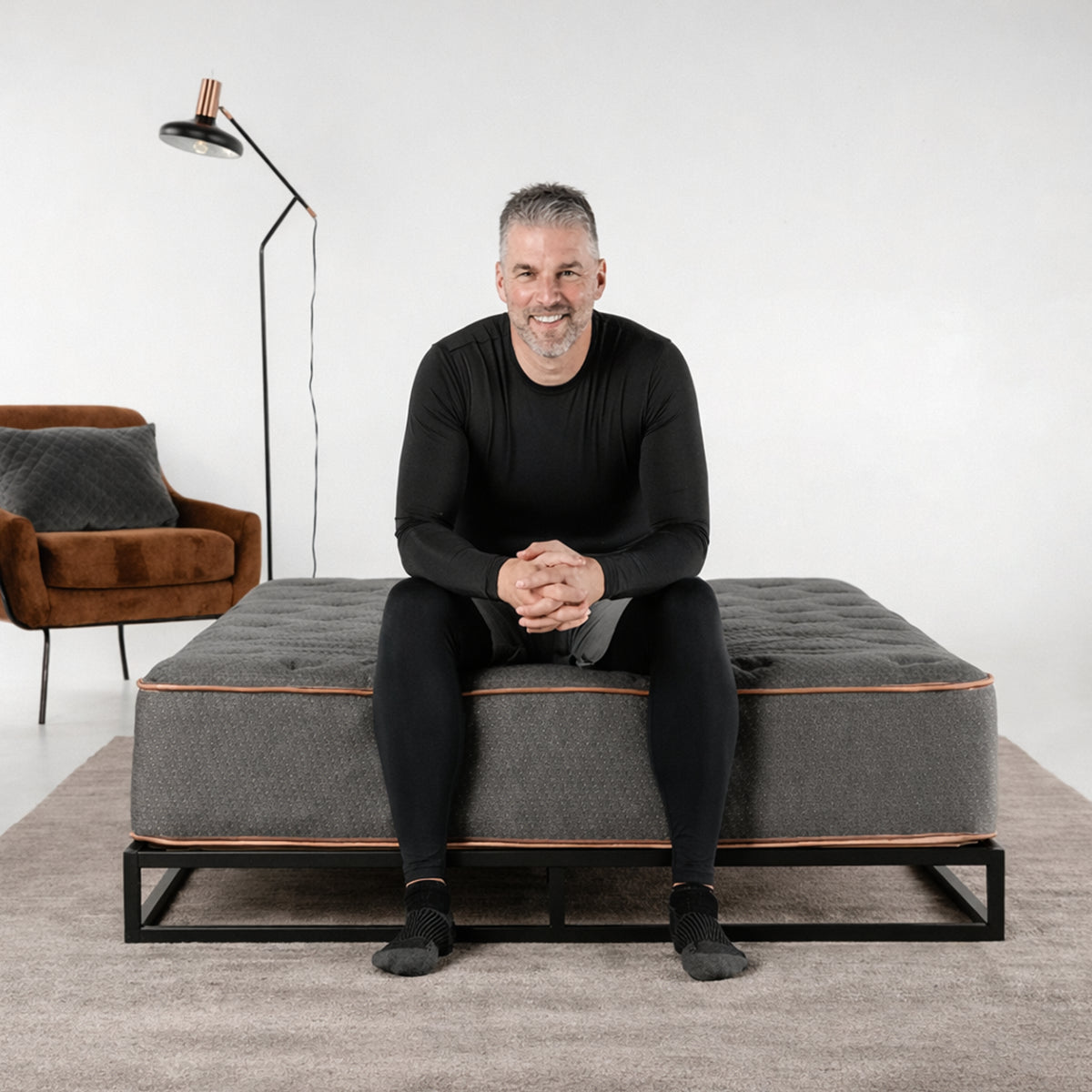 A man sitting on the edge of a Tommie Copper firm hybrid mattress demonstrating superior edge support and stability for active lifestyles.
