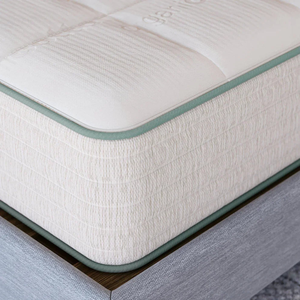 Macro detail shot of the Sage Organic Latex mattress corner showcasing the premium stitching and natural textured fabric with green trim.
