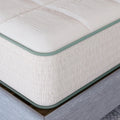 Macro detail shot of the Sage Organic Latex mattress corner showcasing the premium stitching and natural textured fabric with green trim.
