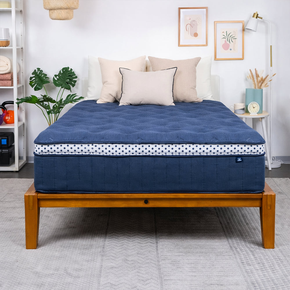 Front-facing view of the WinkBeds Blue 15-inch luxury firm mattress styled on a natural wooden platform bed frame in a bright modern room.
