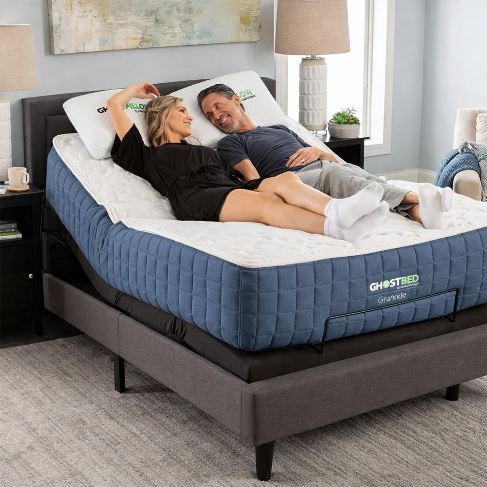 Happy couple relaxing on a GhostBed Grande 14-inch medium mattress with the head section elevated on an adjustable power base.
