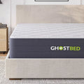 Close-up of the GhostBed Hybrid Mattress side panel and logo, highlighting the premium grey fabric and plush 12-inch profile on a platform bed.
