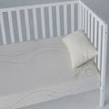White organic cotton fitted crib sheet on a mattress in a white wooden crib for a safe sleep space.
