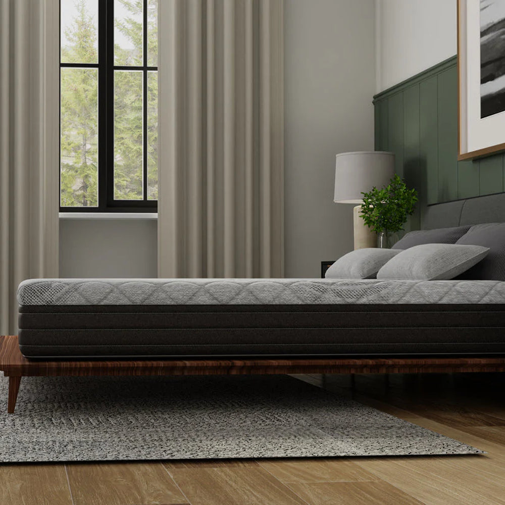 Low-profile side view of the 10-inch thick Essentials mattress by South Bay demonstrating its supportive foam layers on a minimalist wooden frame.
