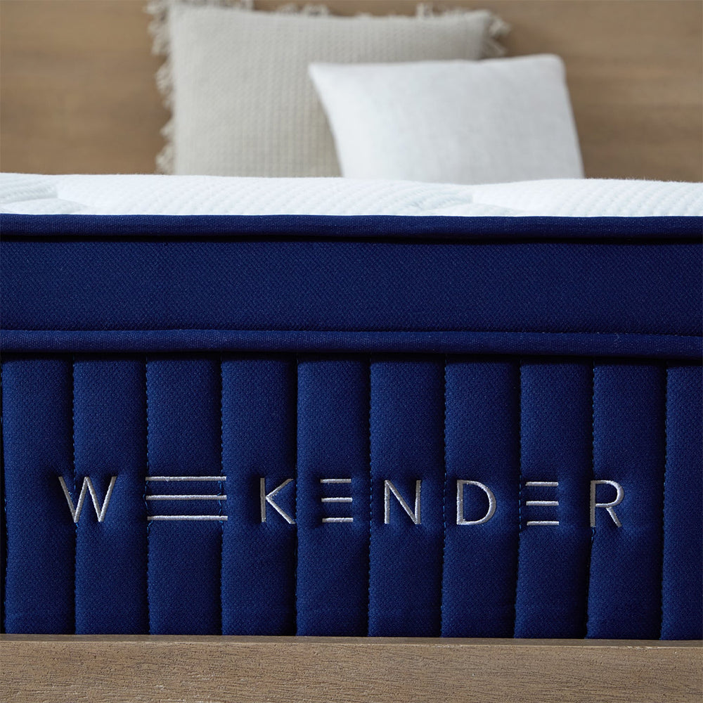 Close-up of the silver embroidered WEEKENDER brand logo on the navy blue luxury fabric side panel of the 13-inch hybrid mattress.
