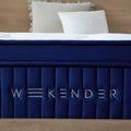 Close-up of the silver embroidered WEEKENDER brand logo on the navy blue luxury fabric side panel of the 13-inch hybrid mattress.
