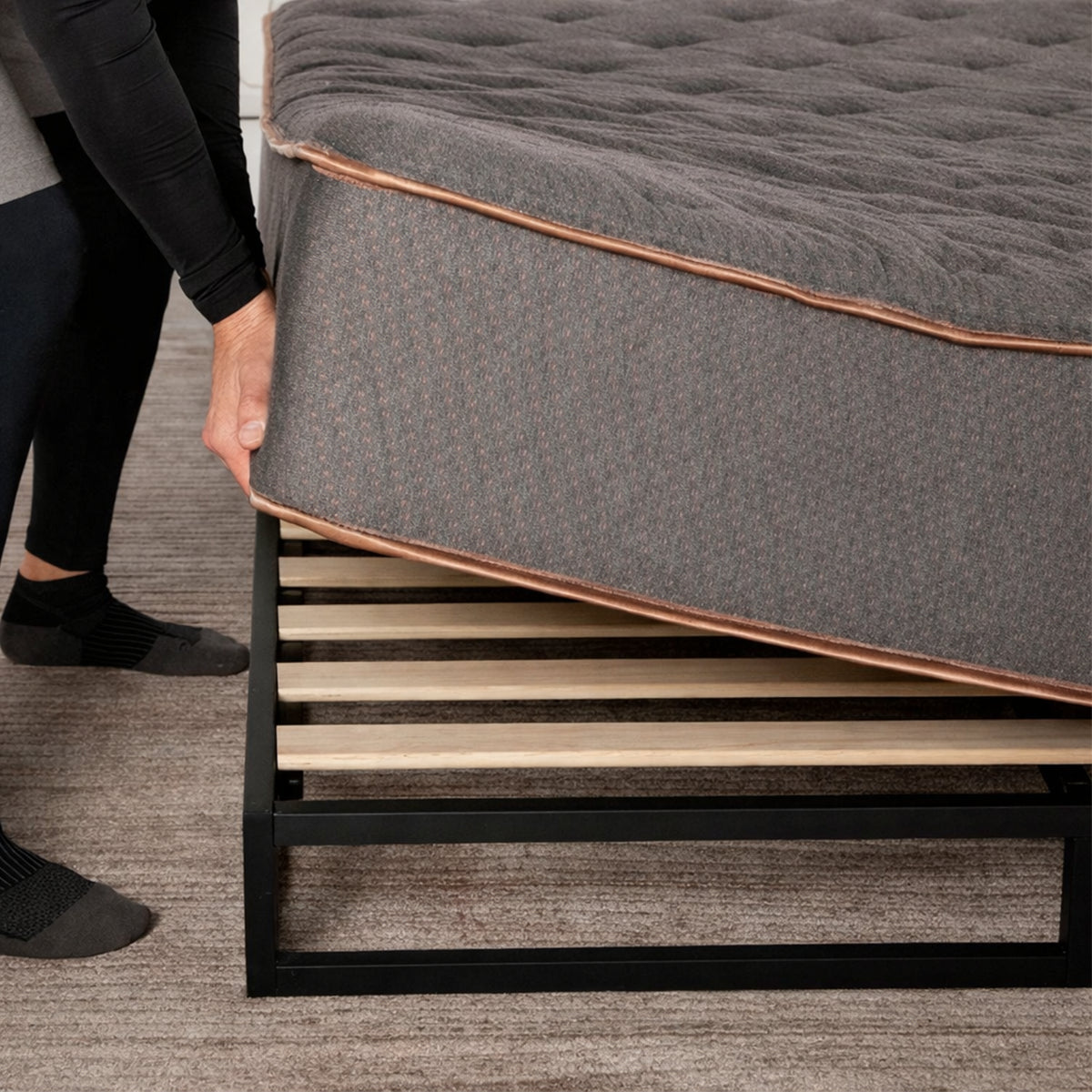 Detailed view of the Tommie Copper Core Znergy hybrid mattress being lifted to show compatibility with a wooden slatted platform bed frame.
