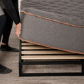 Detailed view of the Tommie Copper Core Znergy hybrid mattress being lifted to show compatibility with a wooden slatted platform bed frame.
