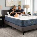 Couple sitting and reading on a supportive GhostBed Grande 14-inch medium mattress in a bright, contemporary bedroom.
