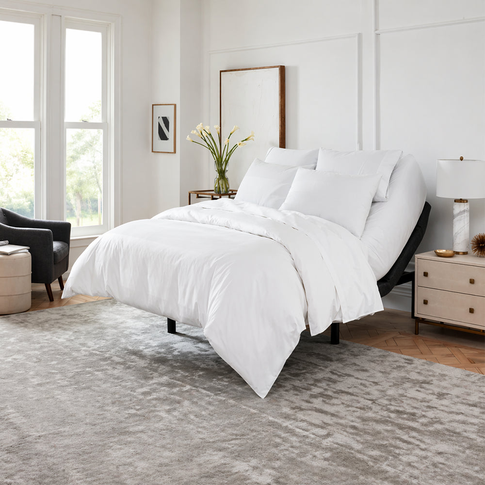 Modern master bedroom featuring the SleepTone S5000 adjustable base with head section elevated, styled with a white duvet on a grey upholstered frame.
