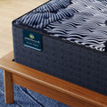 Close-up of Serta Perfect Sleeper X Max branding and quilted surface on a premium wooden bed frame.
