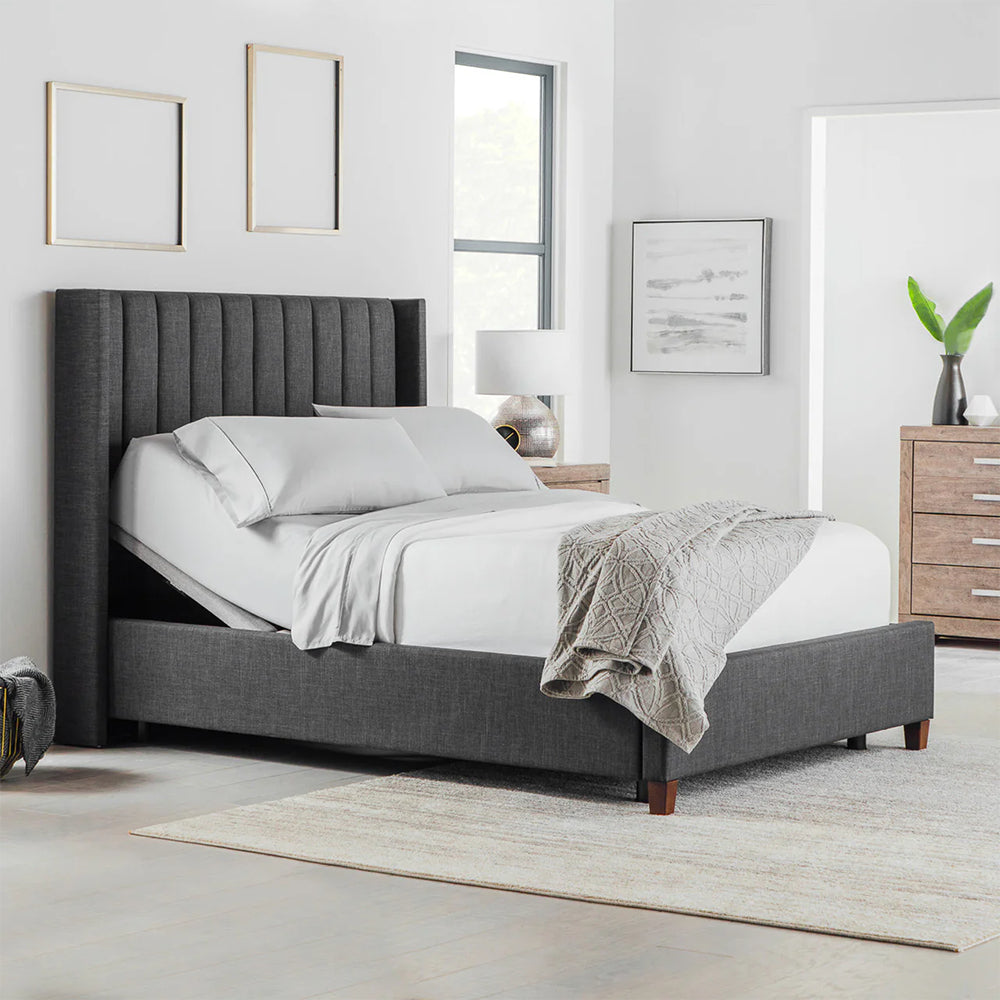 Front perspective of a fully made bed featuring the Malouf S755 adjustable base with head elevation and a charcoal fluted headboard.
