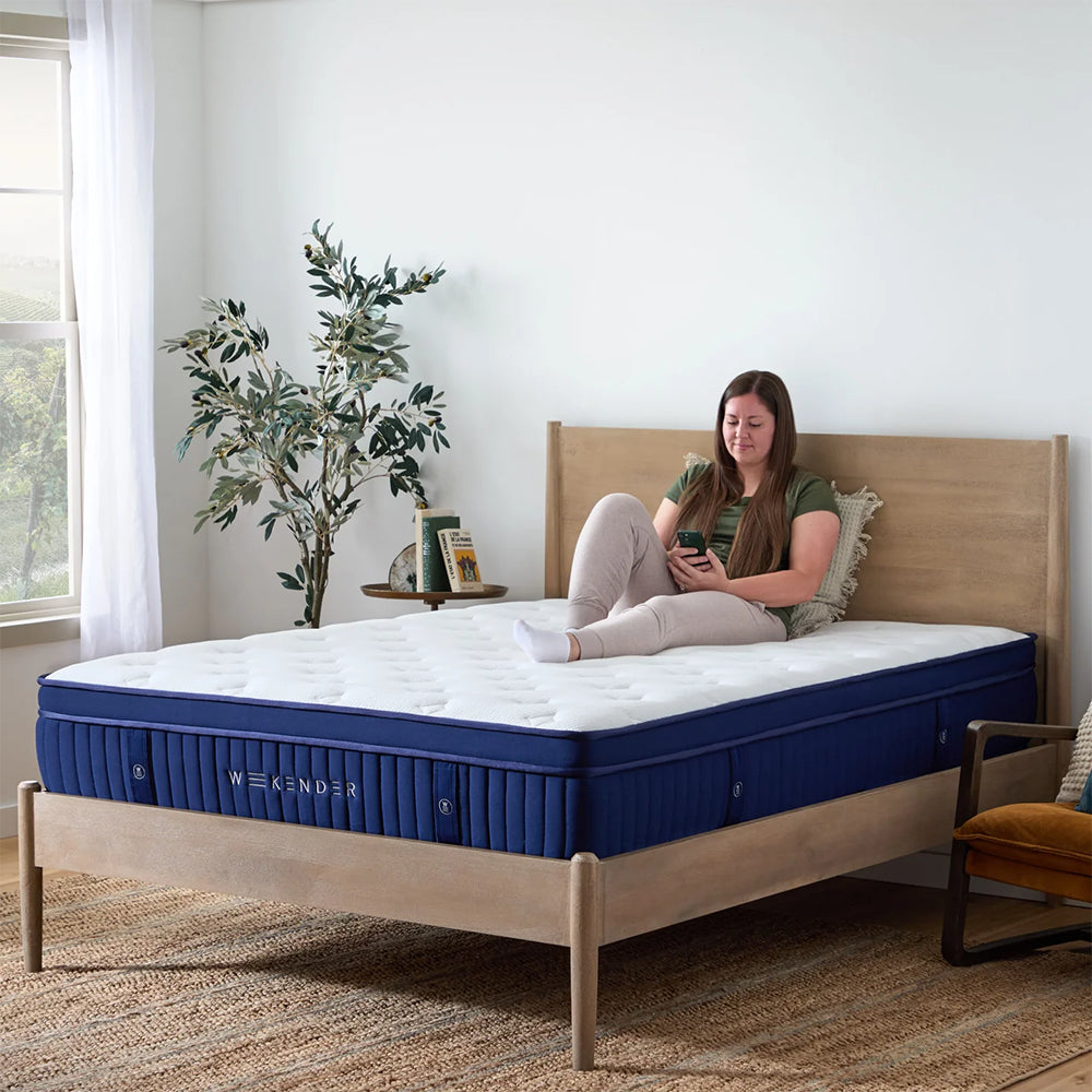 Woman sitting on the edge of the Weekender 13-inch hybrid mattress, demonstrating superior edge support and medium plush comfort.
