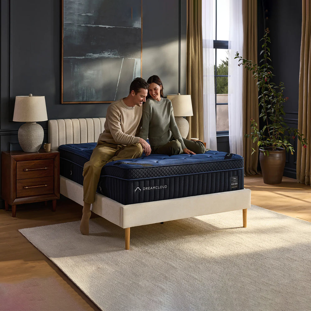 Happy couple sitting on the edge of a DreamCloud Ultra mattress, demonstrating the reinforced edge support and 15-inch luxury profile.
