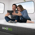 Couple relaxing on a supportive GhostBed RV hybrid mattress in a van, demonstrating the bed's stable surface.

