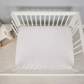 Overhead view of a white Hyper-Linen crib sheet on a mattress for breathable, safe infant rest.
