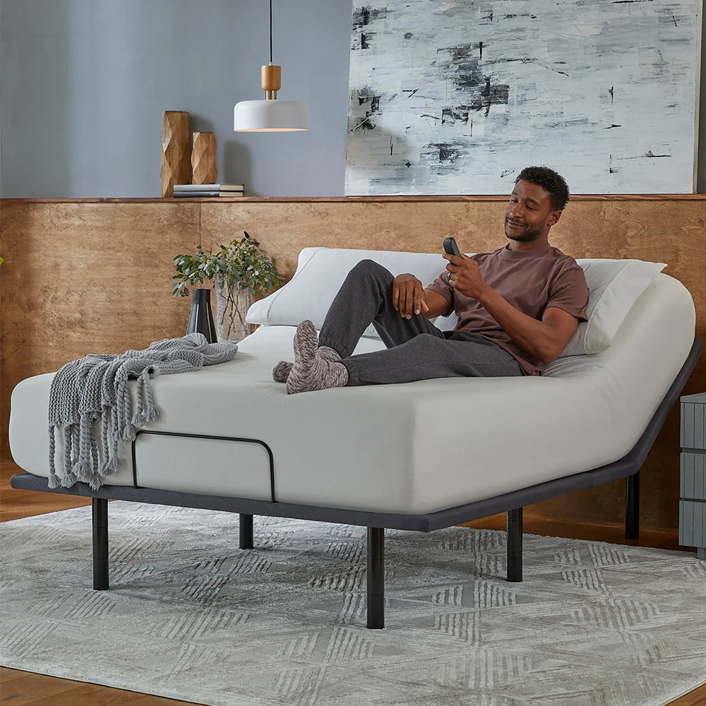Man relaxing on a baselogic Silver Adjustable Base using the wireless remote to adjust his sleep position for personalized comfort.
