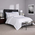 Elegant white hotel luxury sheets with navy blue embroidered stripes on a modern tufted bed.
